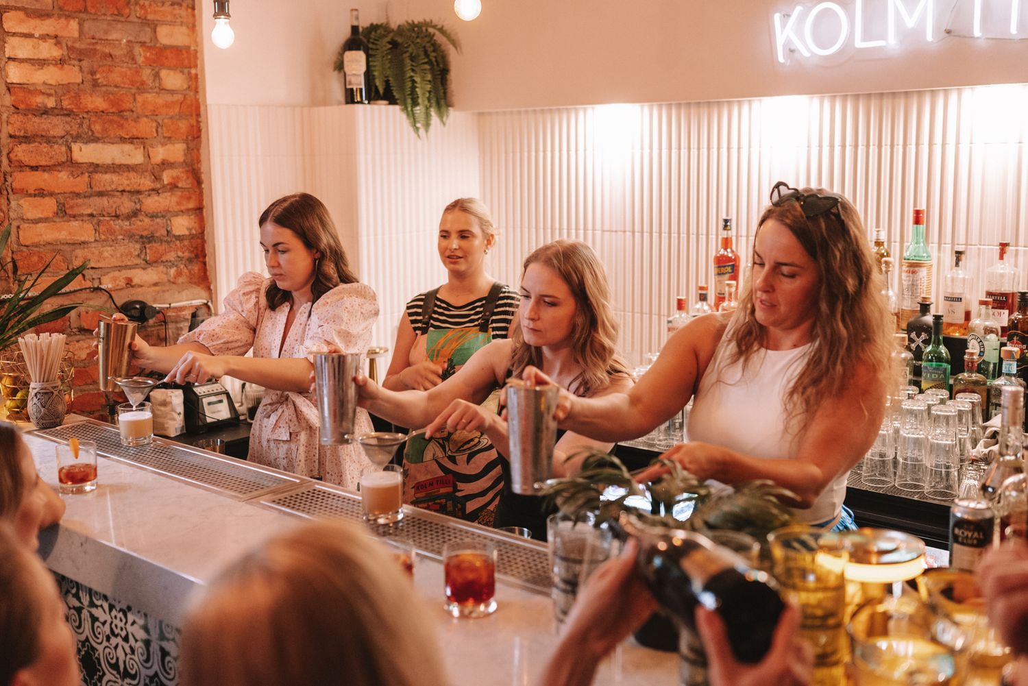 People participating in a cocktail making class at a stylish bar with brick walls and modern lighting.