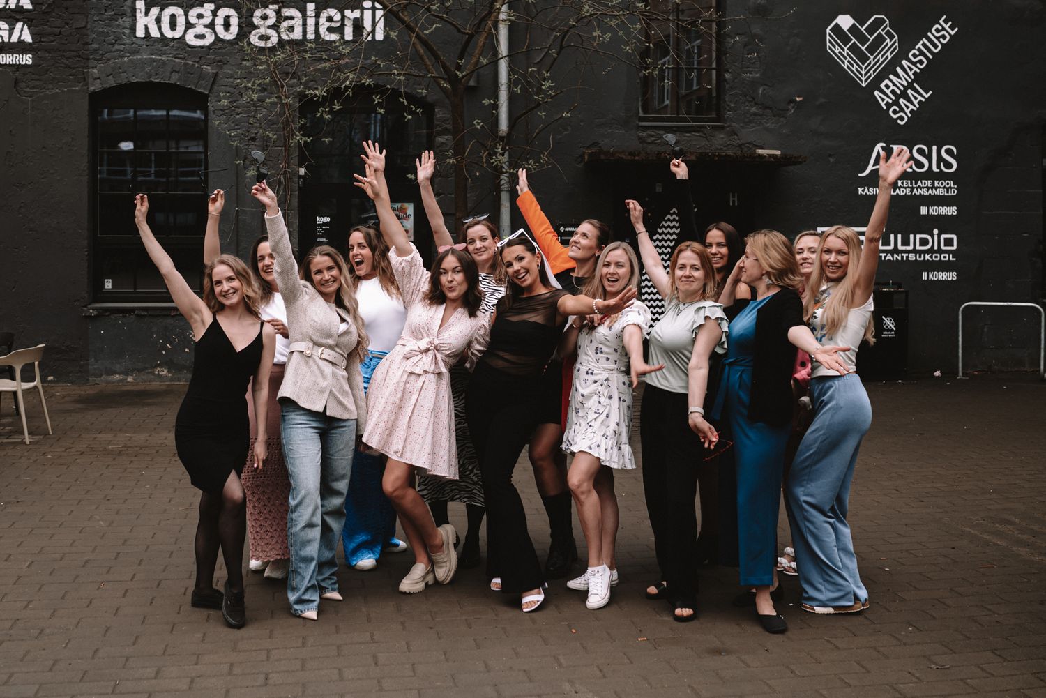 A joyful group celebrates together outside an urban brick building with their arms raised in excitement.