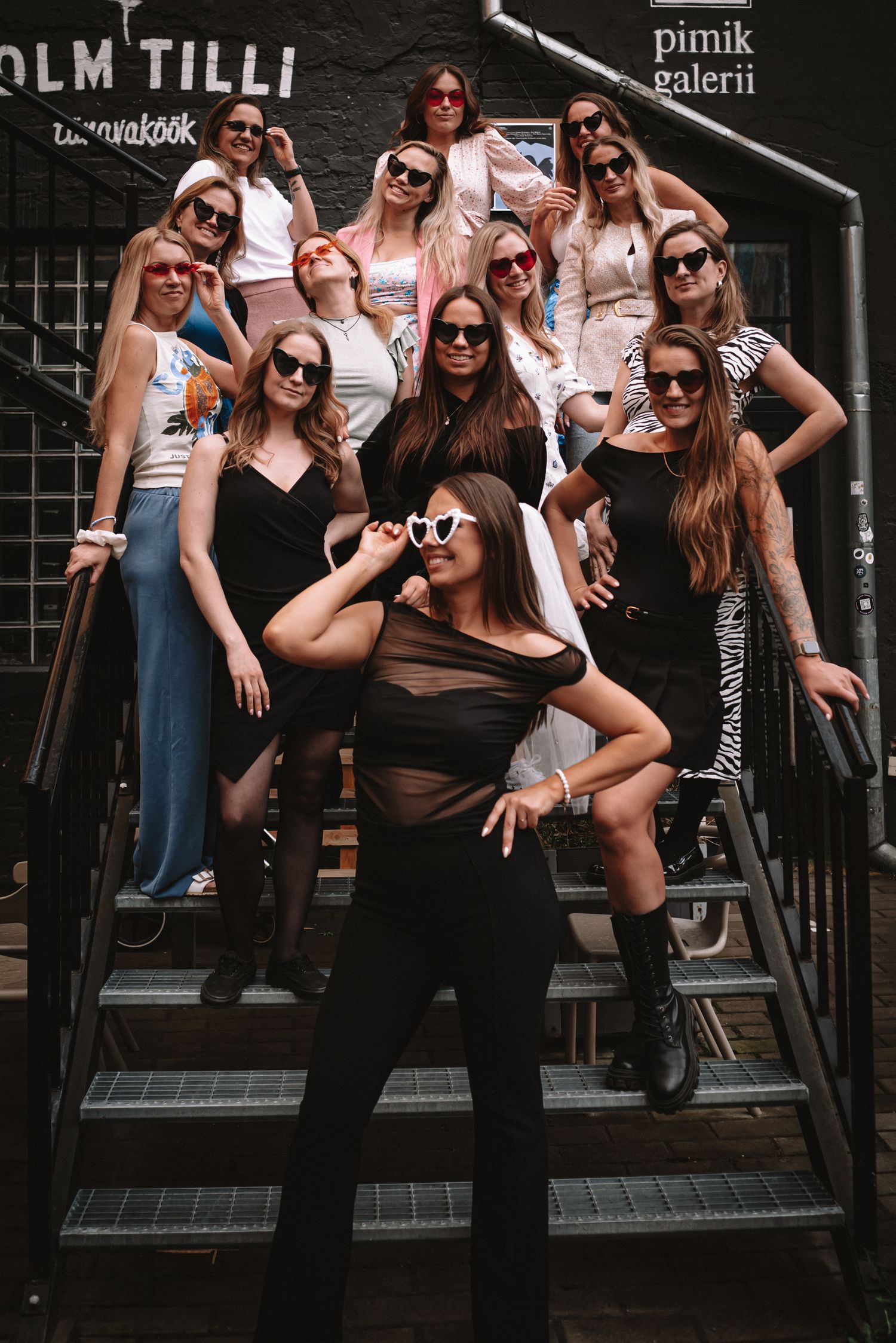 A fashionable group poses on stairs wearing trendy sunglasses and mix of black and white outfits in an urban setting.