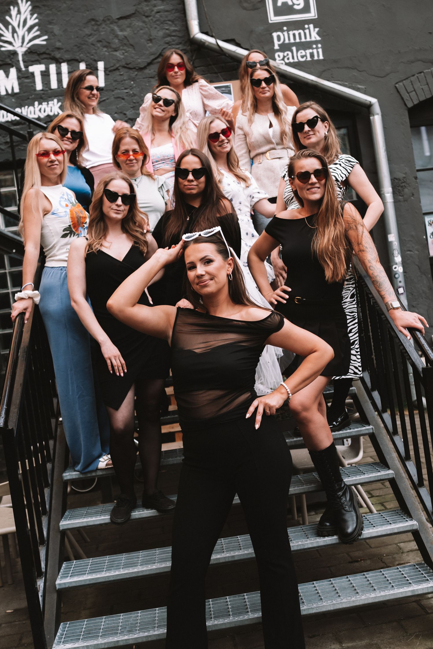 A colorful group photo of friends striking poses on steps wearing sunglasses and fashionable outfits.