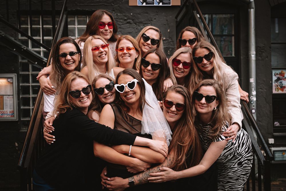 A group of people wearing sunglasses pose together on stairs for a fun group photo.