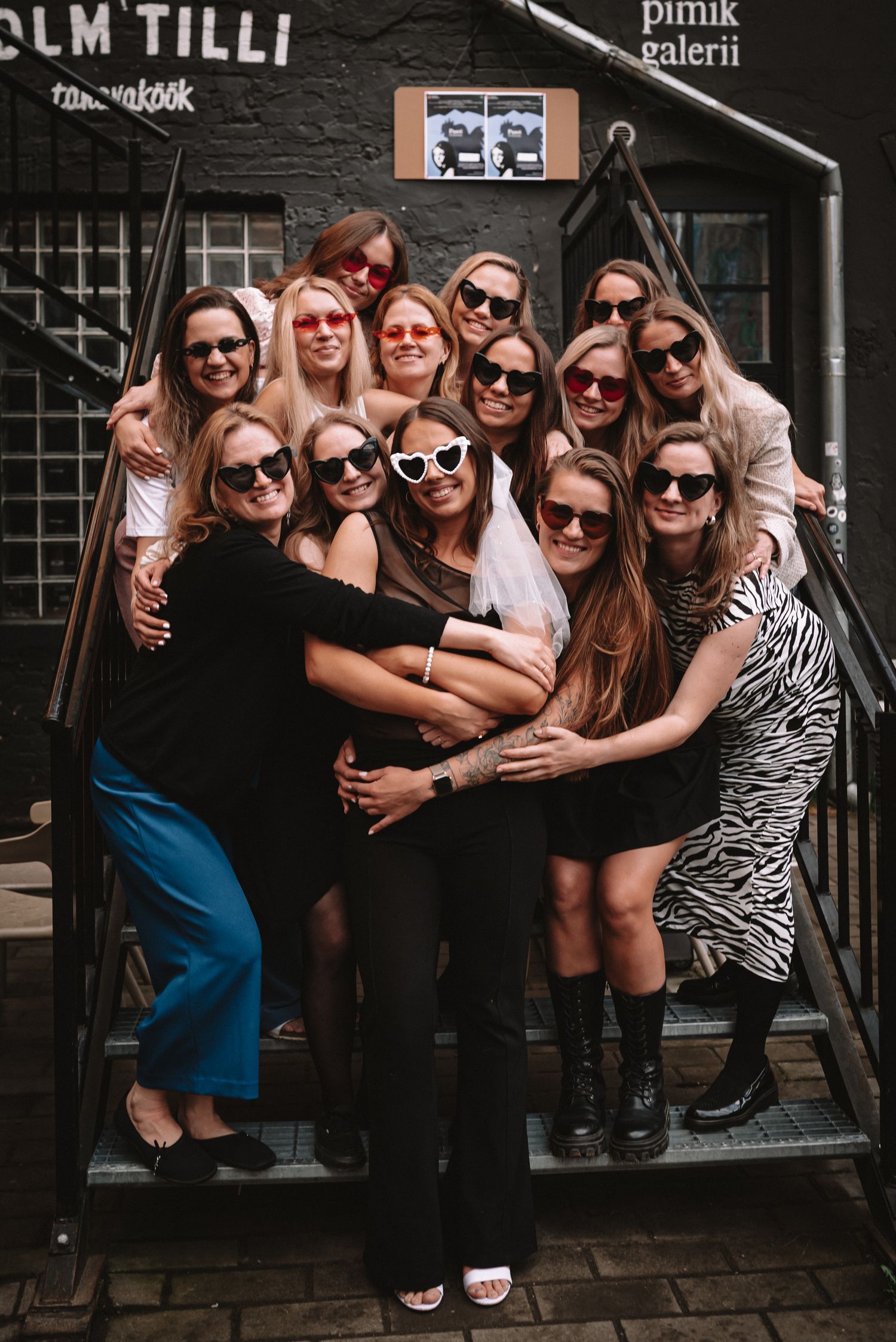 A group of friends wearing sunglasses pose together on outdoor steps in coordinated black and white outfits.