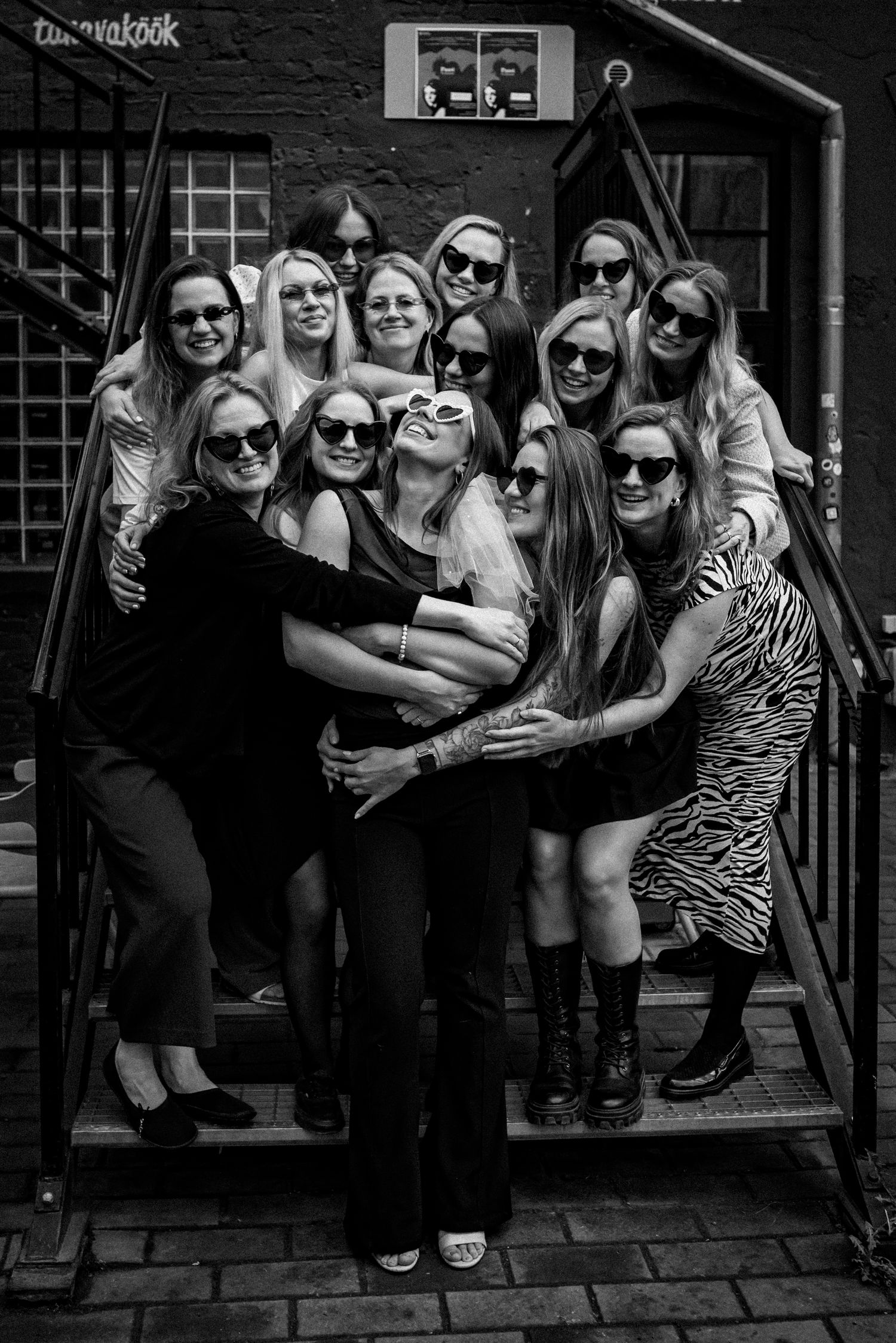 A black and white photograph of a group wearing sunglasses gathered together on outdoor steps.