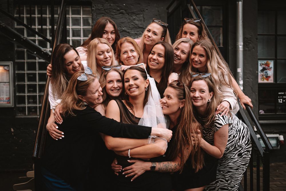A group of people huddle together smiling and laughing in a candid photo against a dark wall.