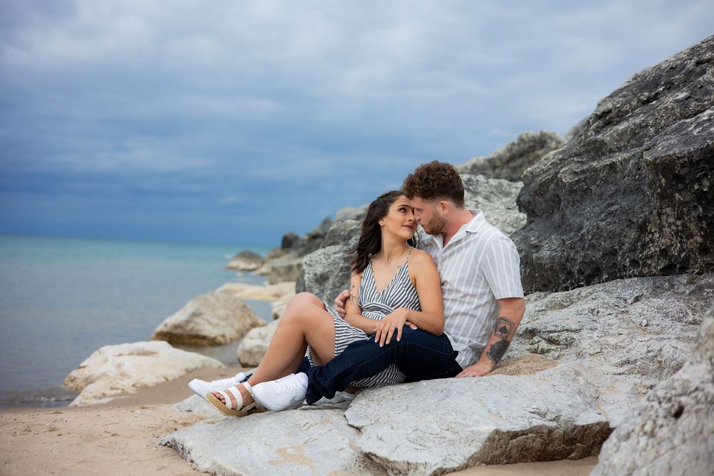 A couple enjoys a romantic moment on rocky coastal cliffs overlooking the ocean at sunset.