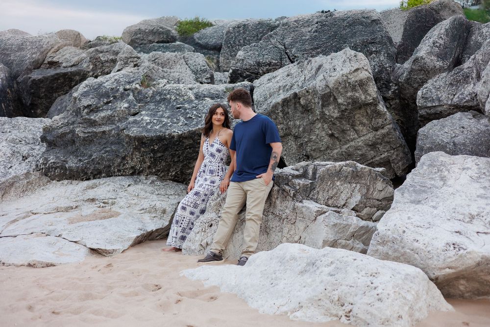 Couple sitting together on large coastal rocks near the ocean during a sunny day at the beach.