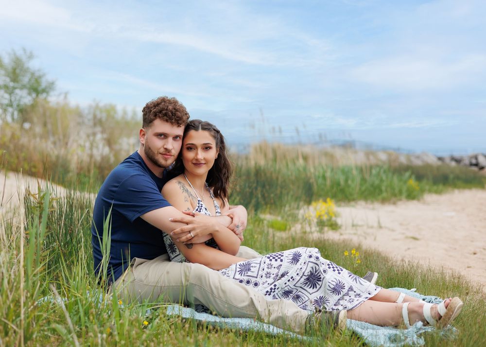 A couple enjoys a romantic picnic on a grassy beach as they relax together on a blanket during a sunny afternoon.