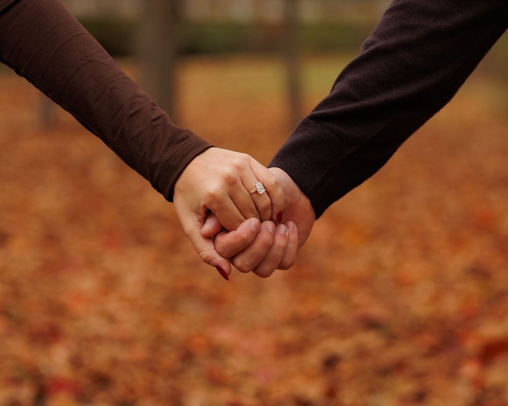 Two people hold hands while walking through vibrant autumn leaves scattered on the ground.