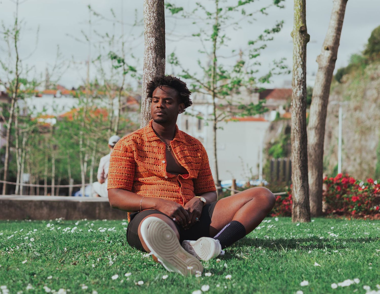 Person in orange shirt sitting on grass with trees in background.