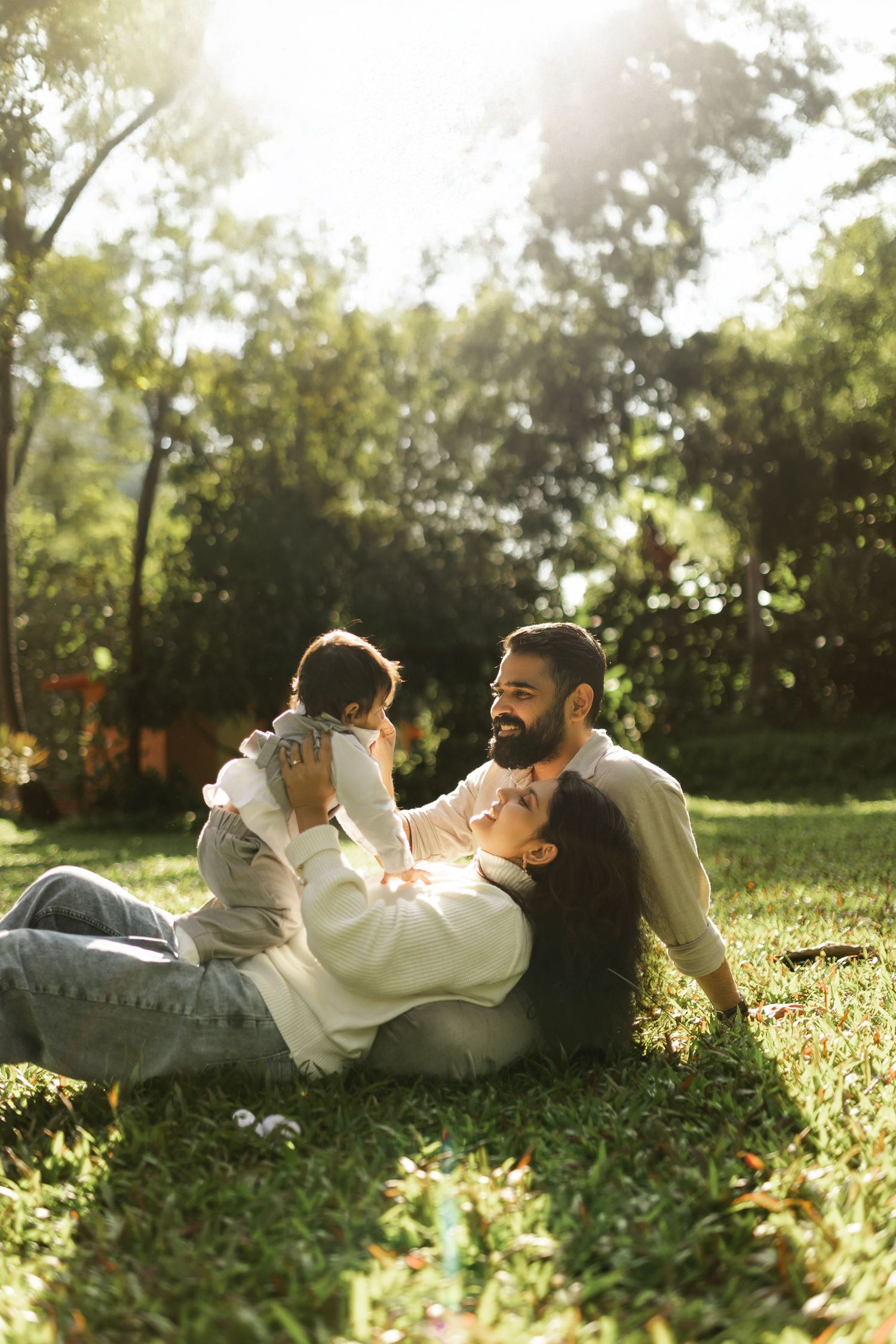 Happy family enjoying a playful moment together on grass in a sunlit backyard garden on a warm afternoon.