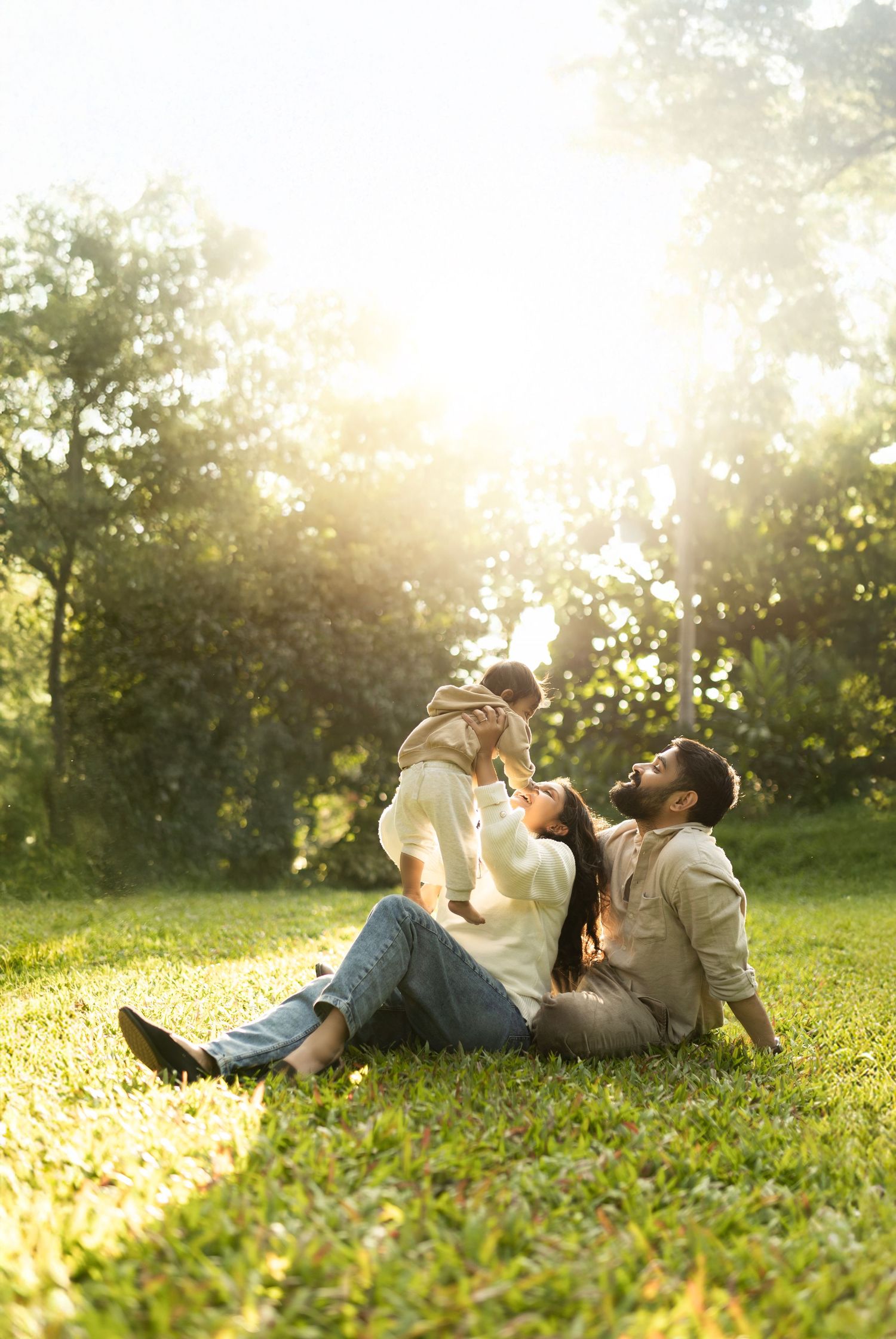 Candid family moment captured in a sunlit park with golden sunburst through trees on a warm afternoon.