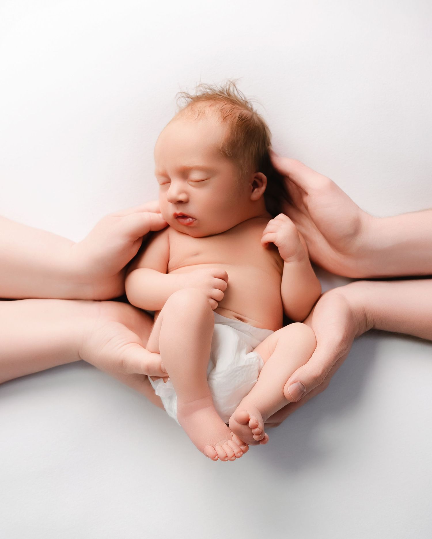 Peaceful sleeping newborn cradled gently by adult hands against white background in diaper.