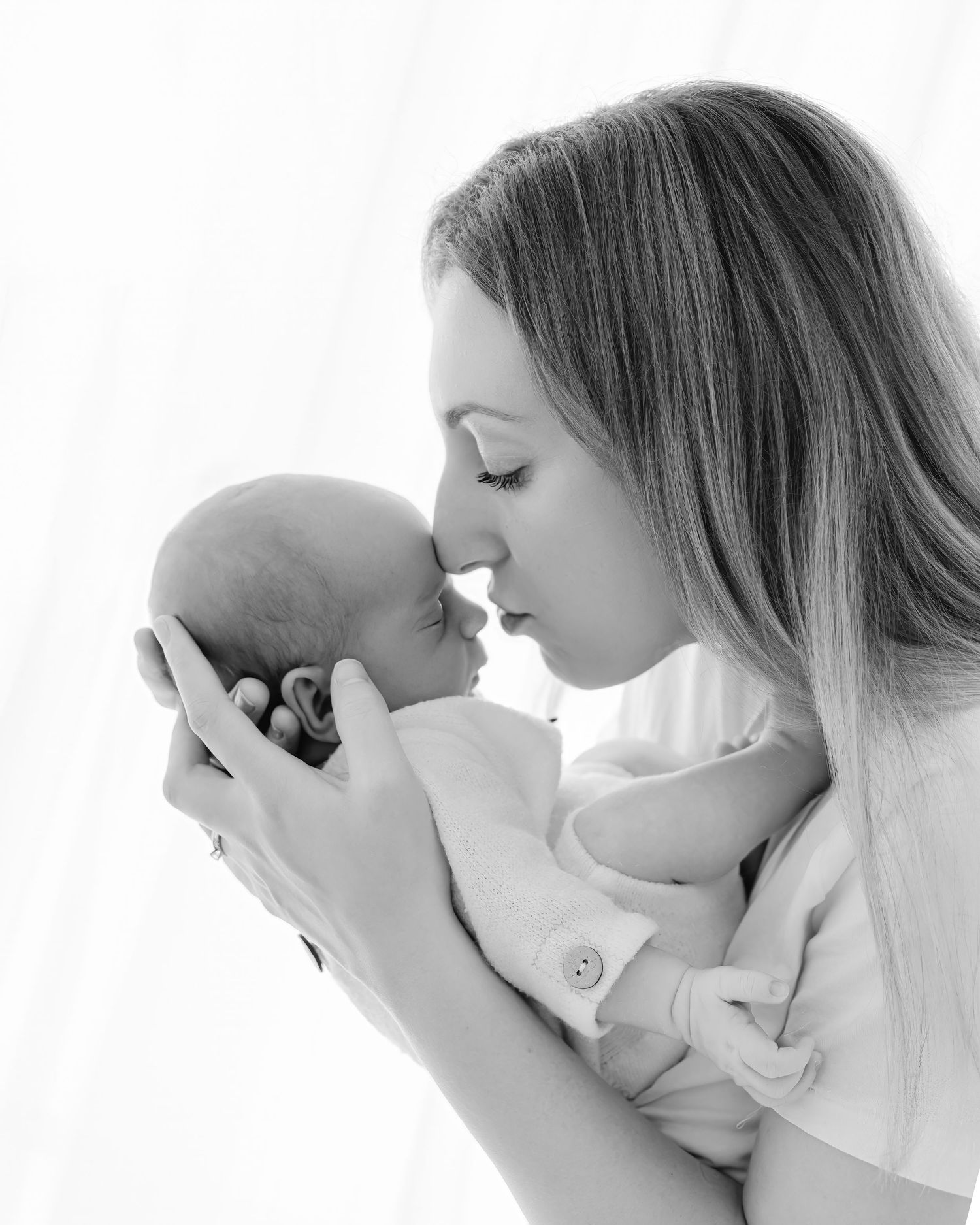 Series of black and white photos showing tender moments between parent and baby in soft, intimate poses.
