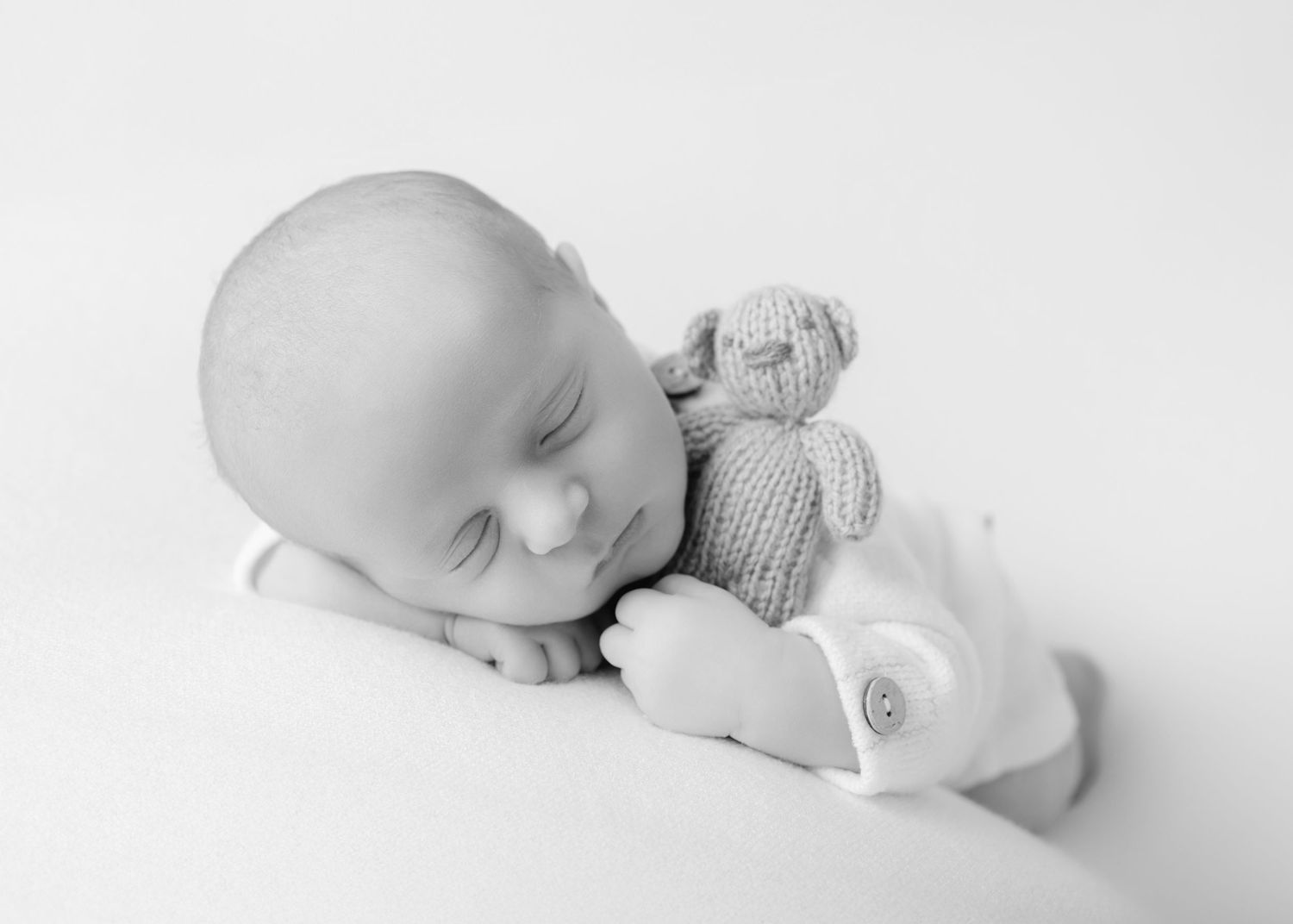 Precious newborn baby sleeping peacefully with teddy bear in monochromatic artistic portrait series.