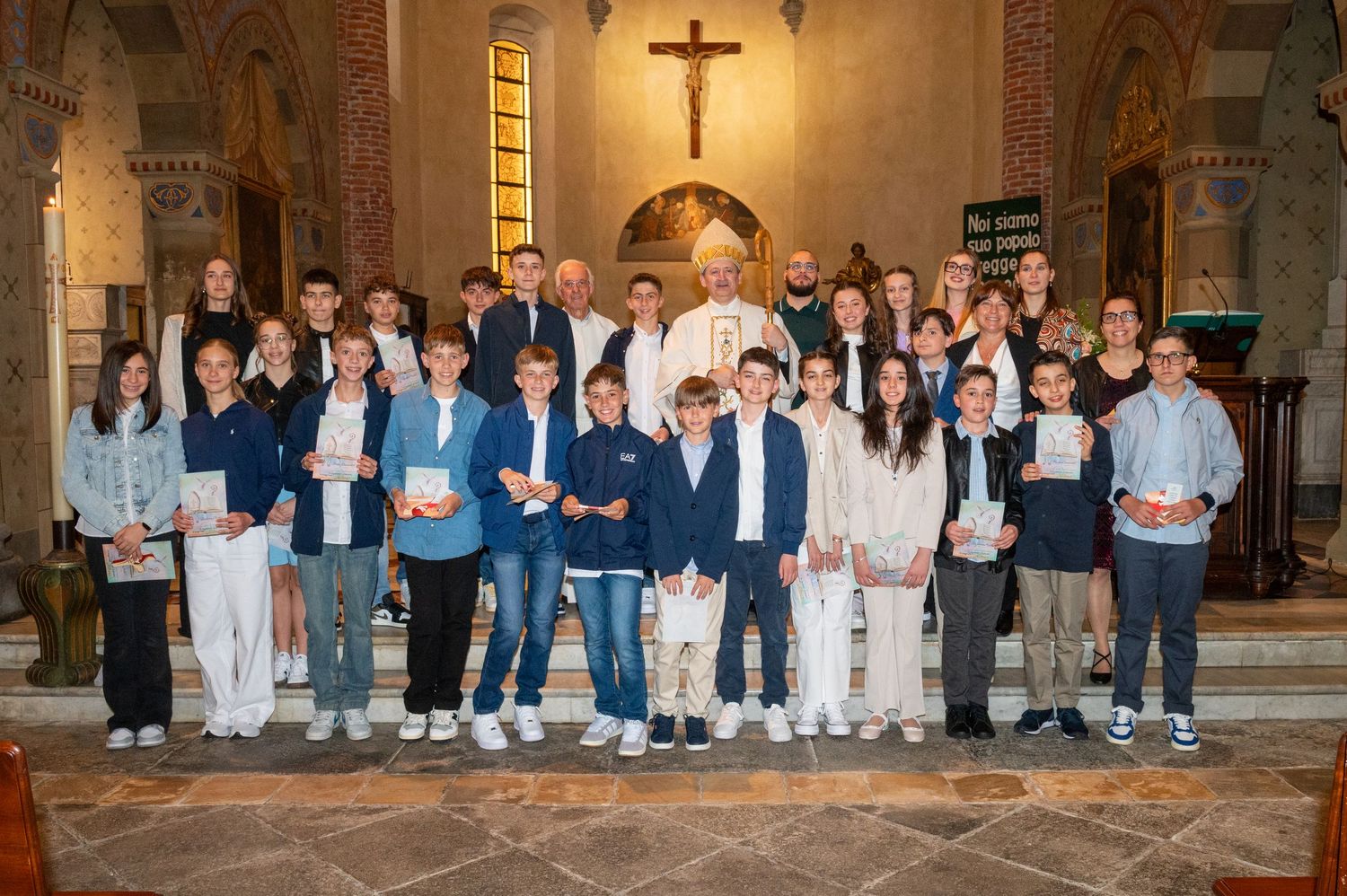A group stands together in front of an altar with a crucifix in a traditional church setting.