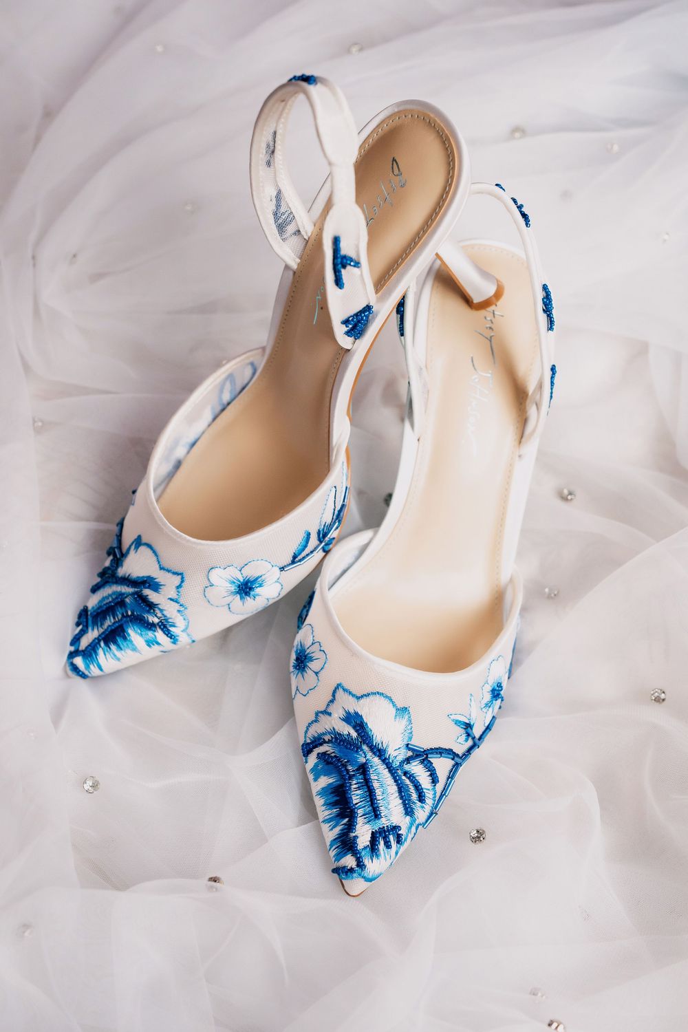 Elegant white high heel shoes with blue floral pattern design rest on soft white tulle fabric.