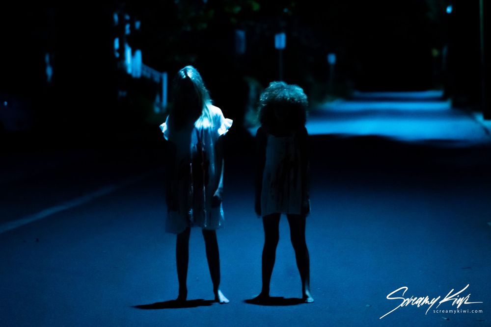 Two silhouettes of people standing on a dark street illuminated by ethereal blue lighting at night.