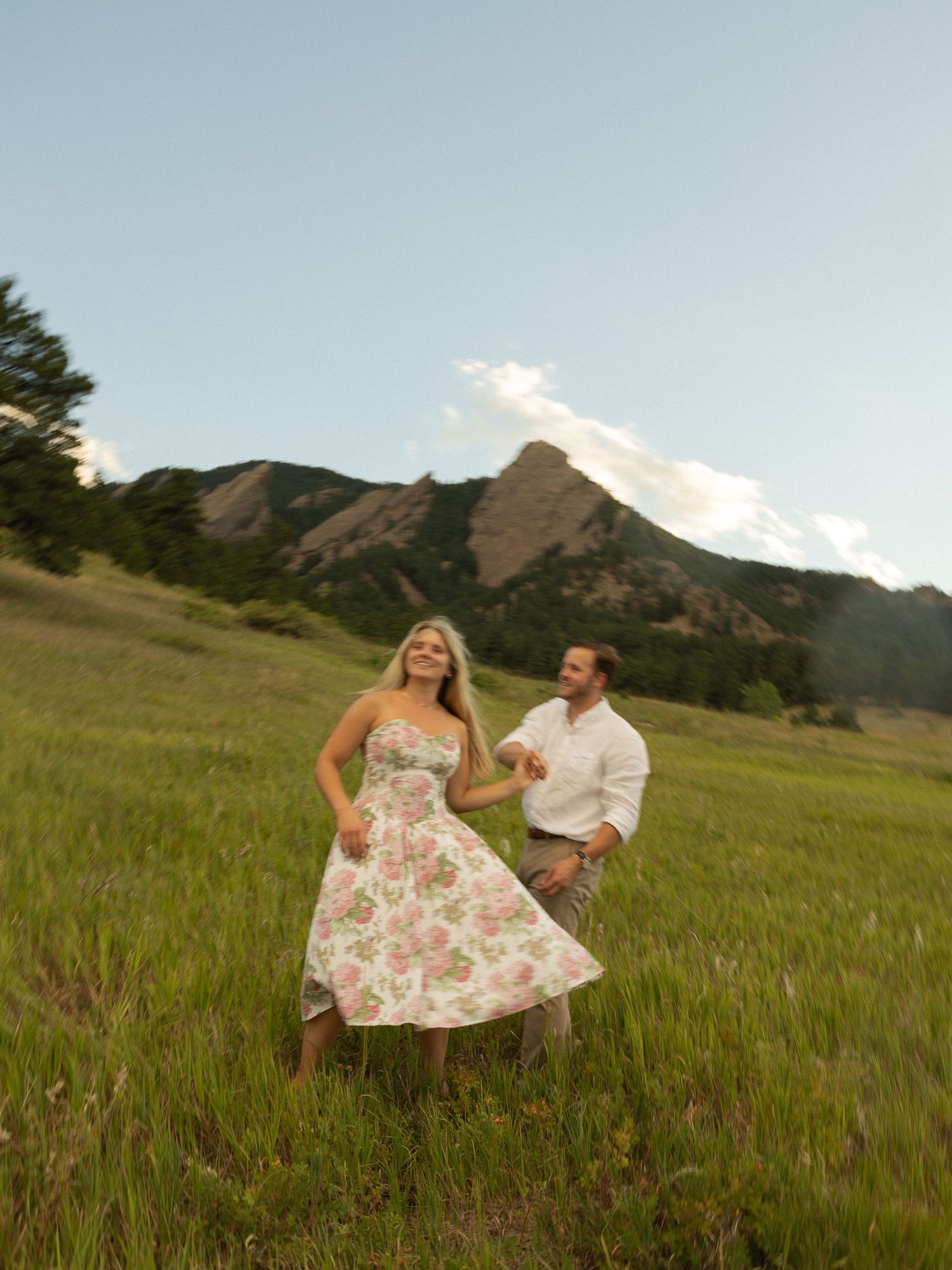 A couple enjoys a romantic moment in a grassy meadow with the Flatirons rock formation in Boulder, Colorado as their backdrop.