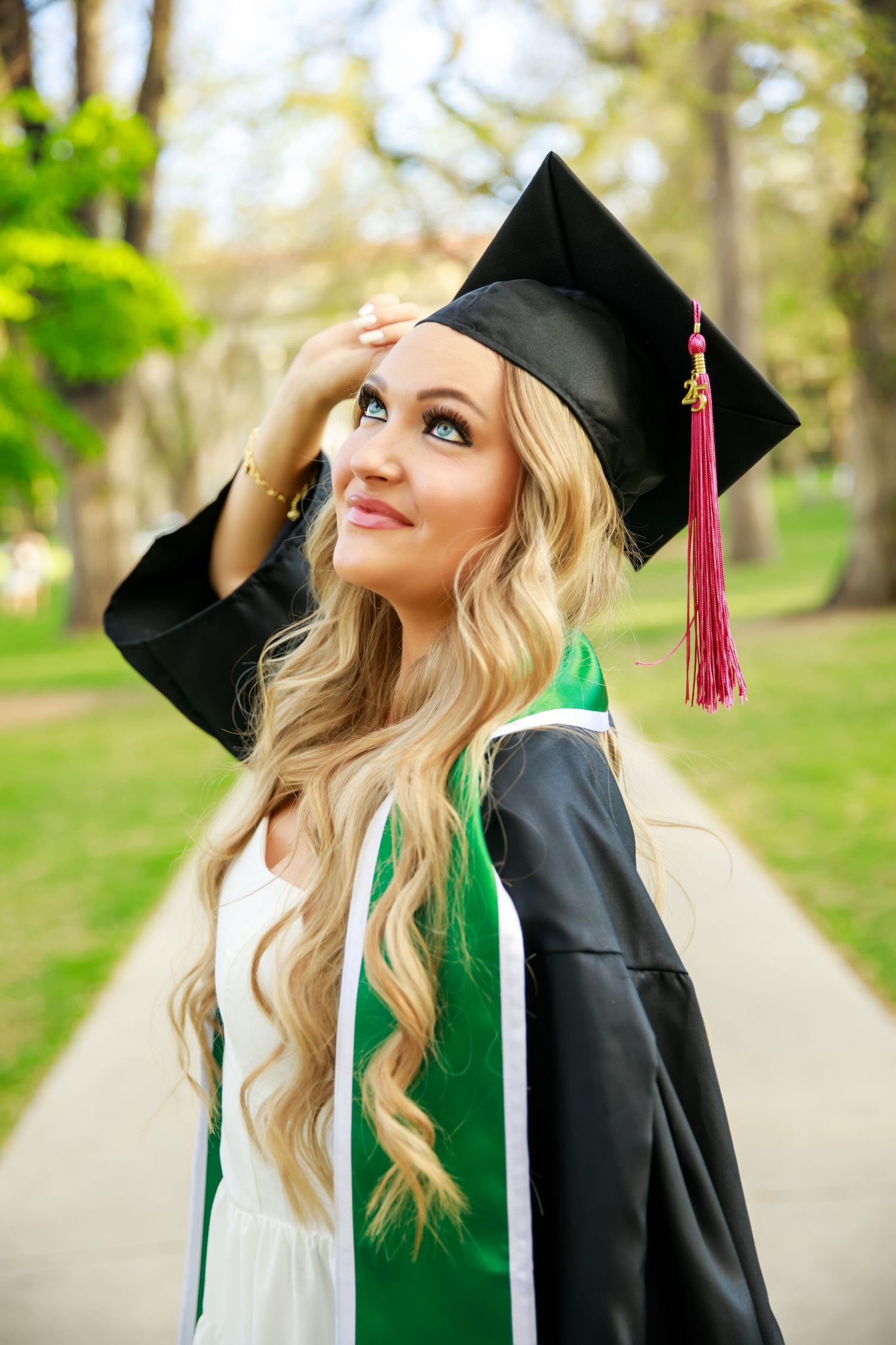 Graduate in cap and gown looking up thoughtfully outdoors.