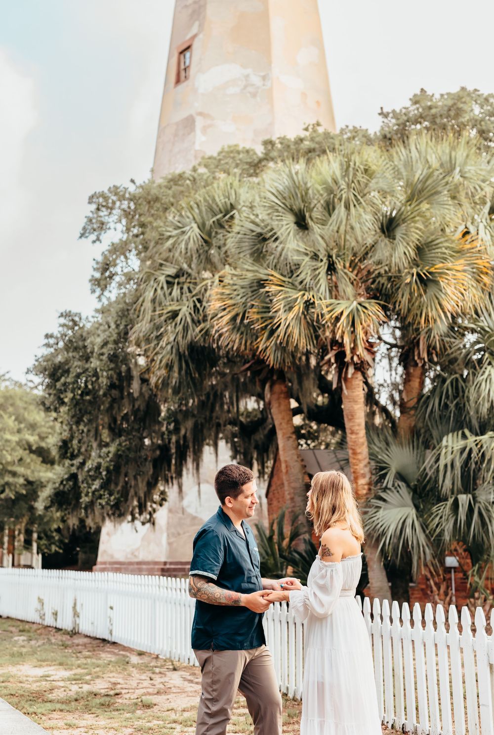 Couple standing near a lighthouse with palm trees and Spanish moss in the background.
