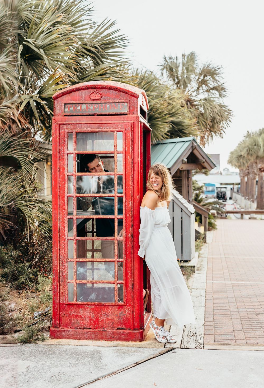 couple at a red British phone booth with tropical palms in background. Bald head island north carolina.