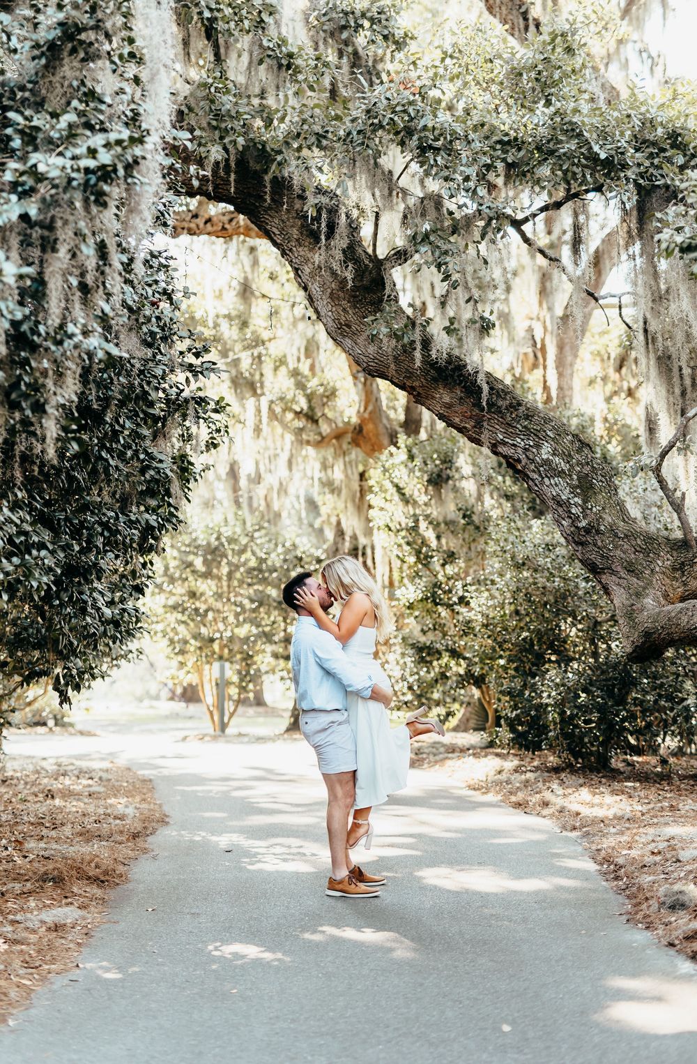 Couple embracing under Spanish moss draped trees on garden path.
