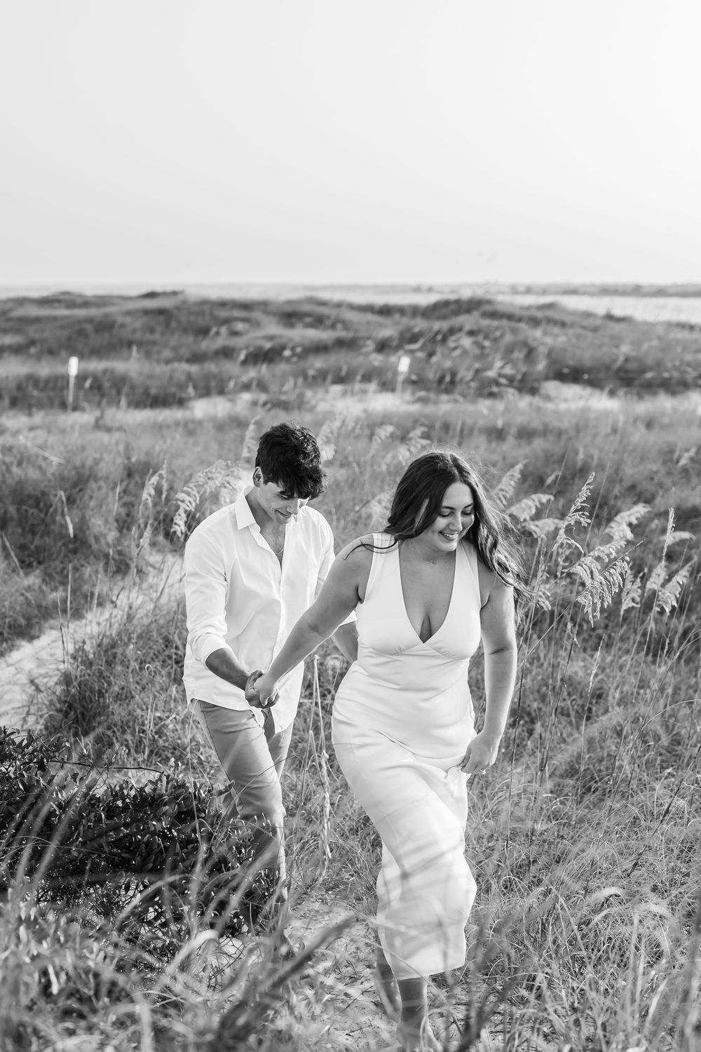 A couple walking through tall grass on a coastal hillside in black and white.