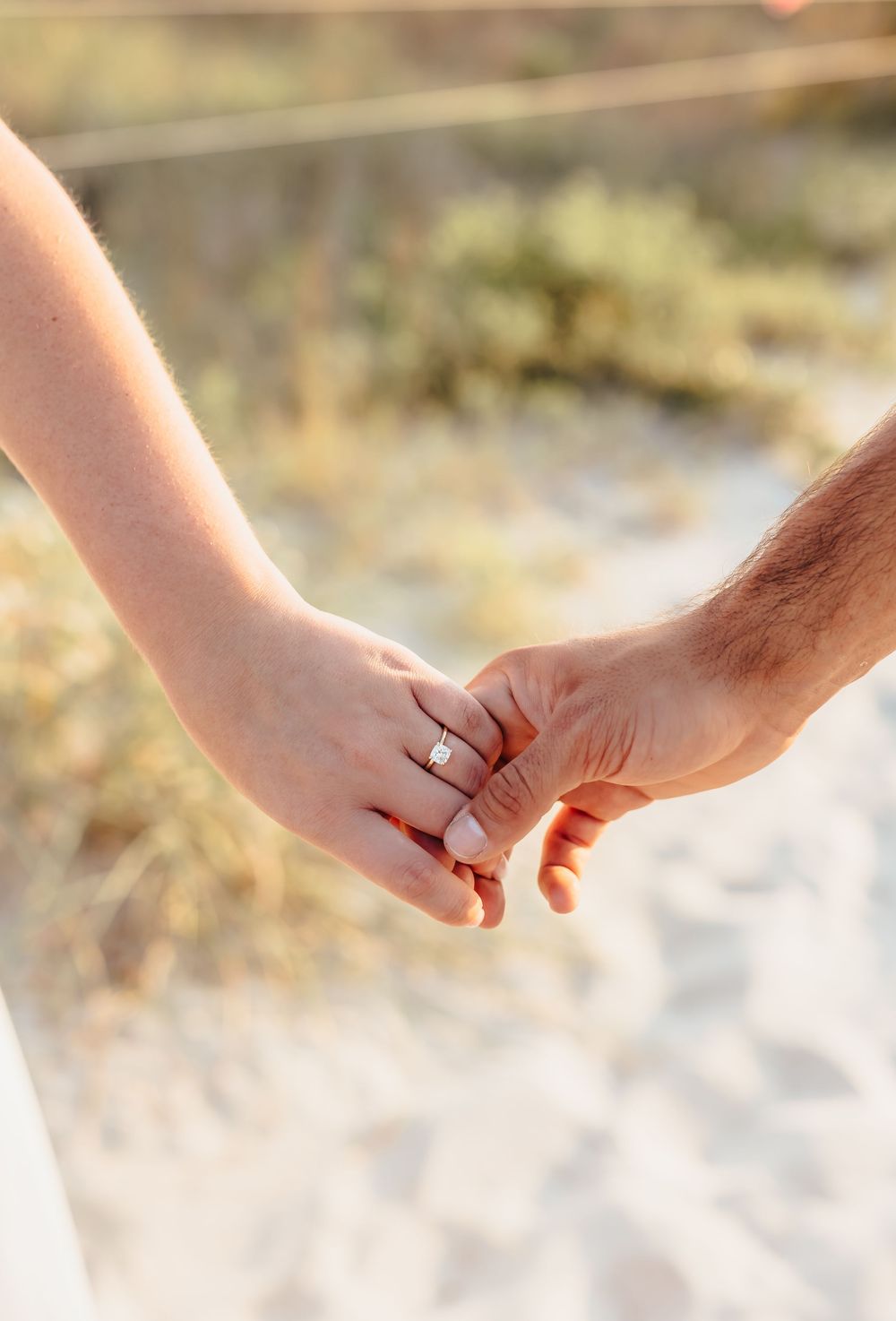 Close-up of hands holding with engagement ring visible in soft natural lighting.