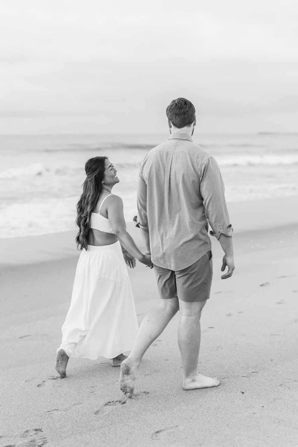 Black and white photo of couple walking along empty beach at sunrise. Wilmington NC.