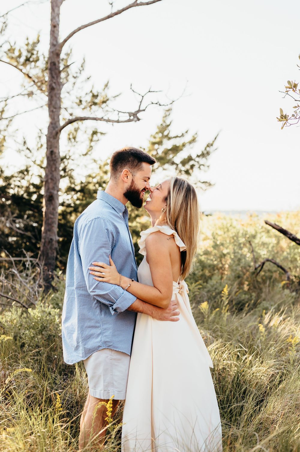 A romantic moment between a couple embracing outdoors under tree branches at sunset.
