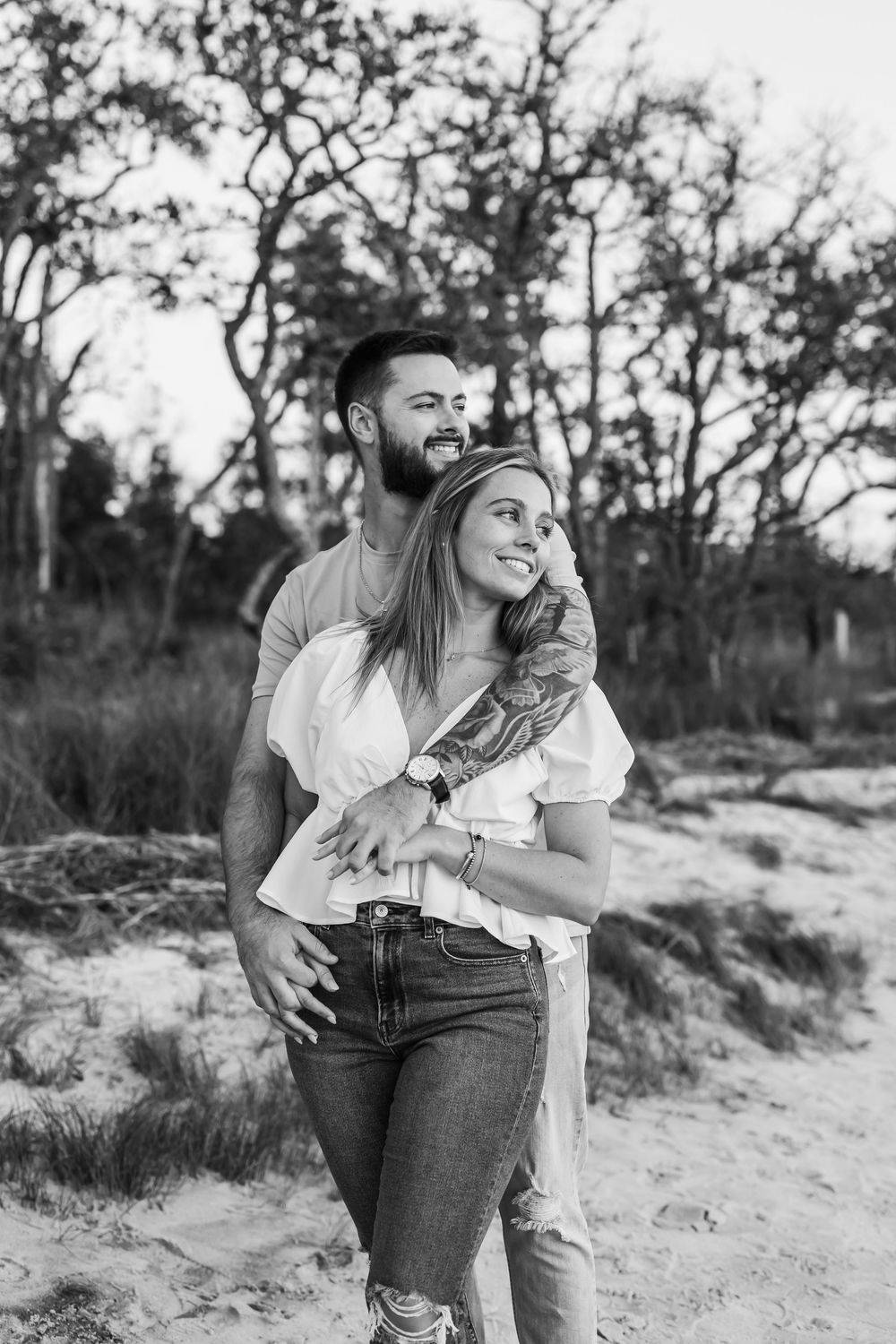 A joyful black and white portrait of a couple embracing on a sandy path.