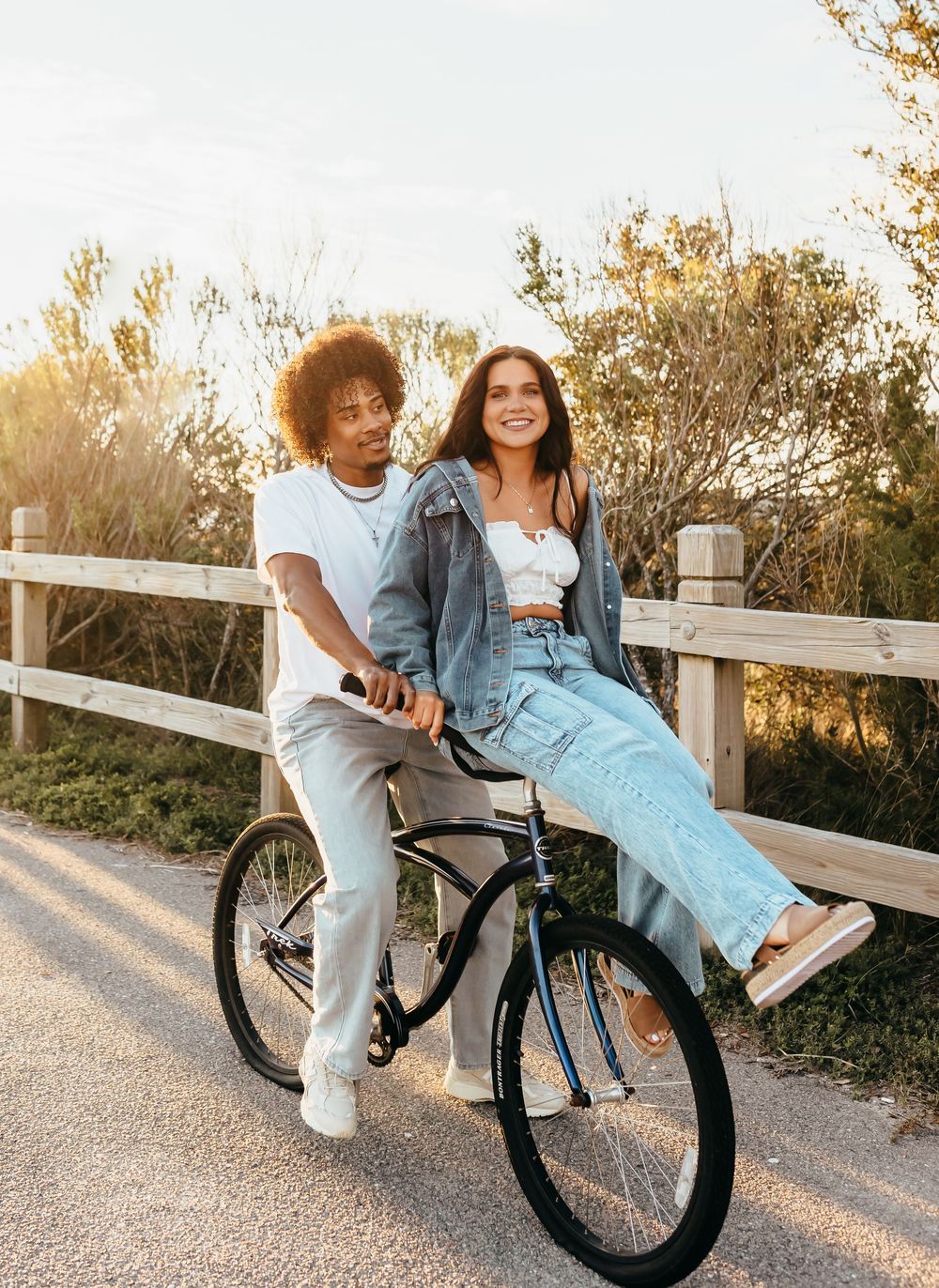 Couple sharing a playful moment on a bicycle along a scenic pathway at sunset.