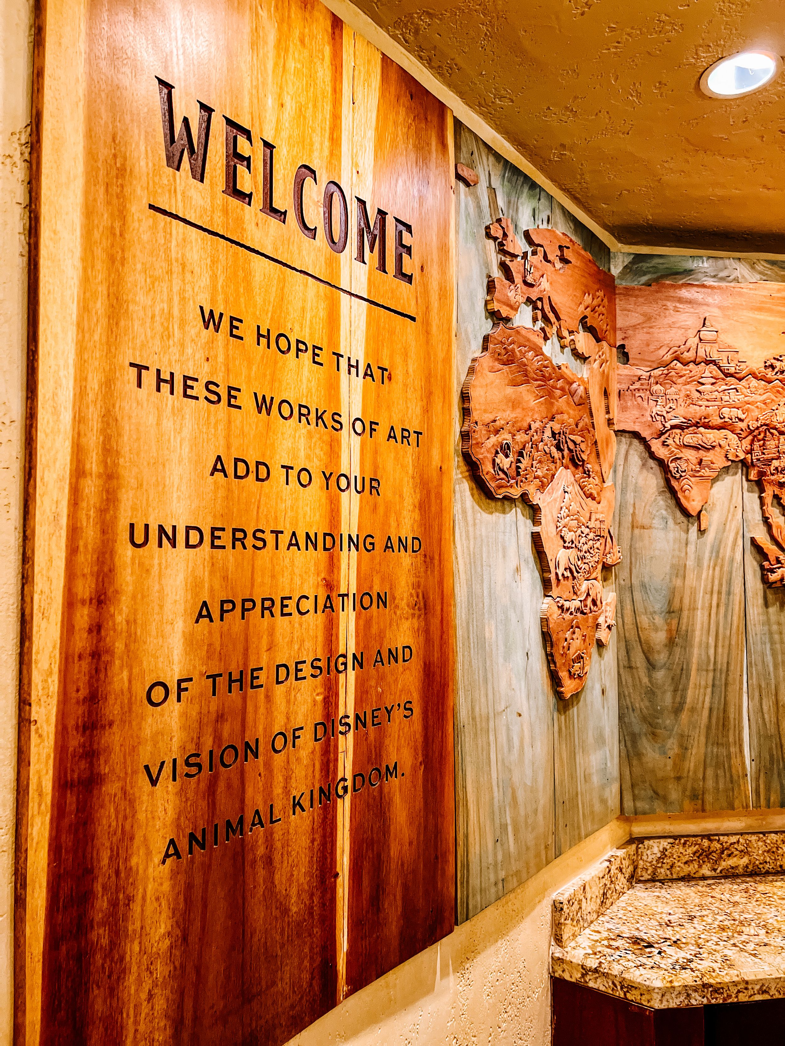 Wooden wall with engraved welcome message and textured world map design at Tiffins restaurant.