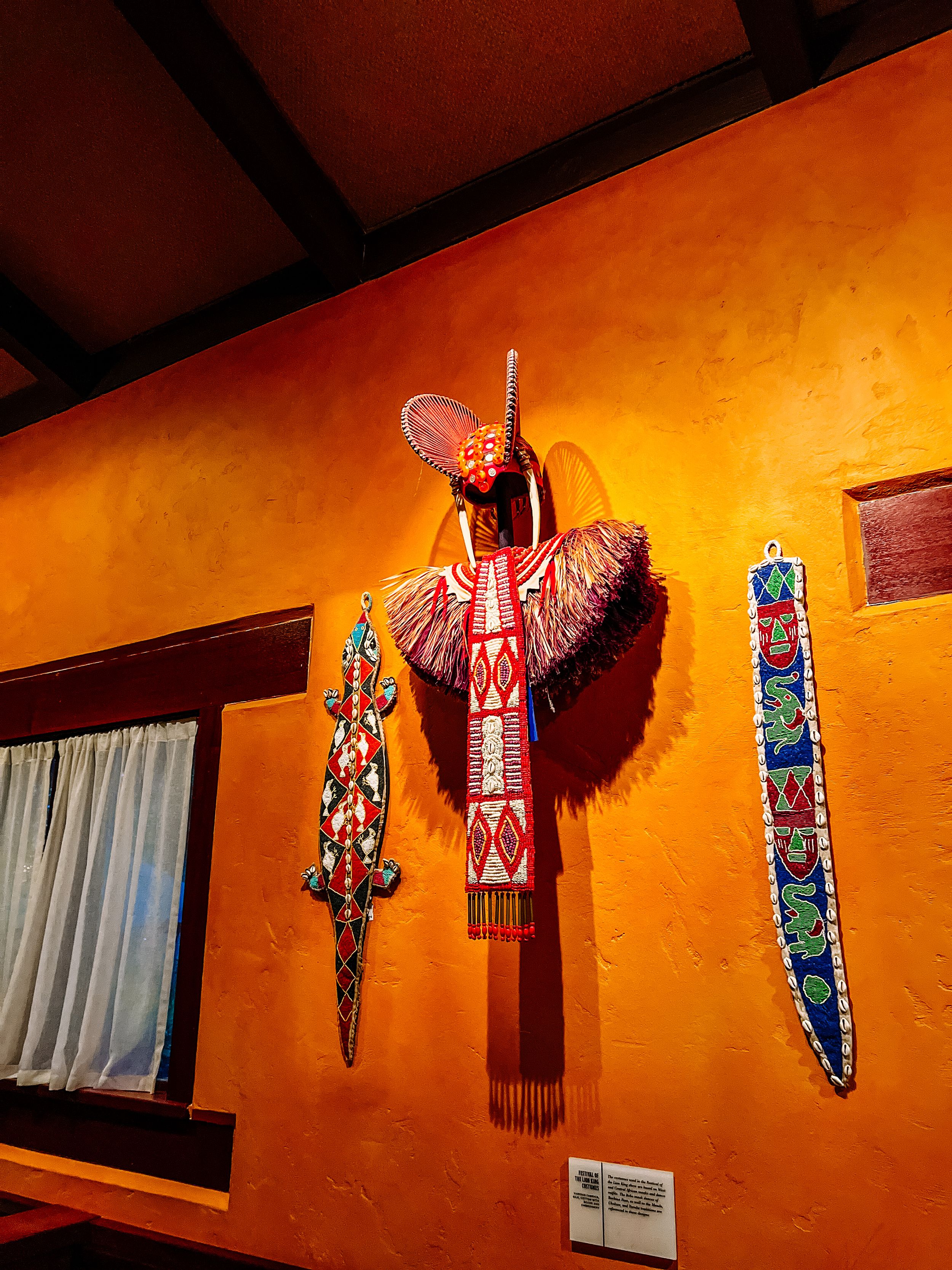 Decorative tribal-inspired masks and artwork illuminated on orange walls in restaurant interior.