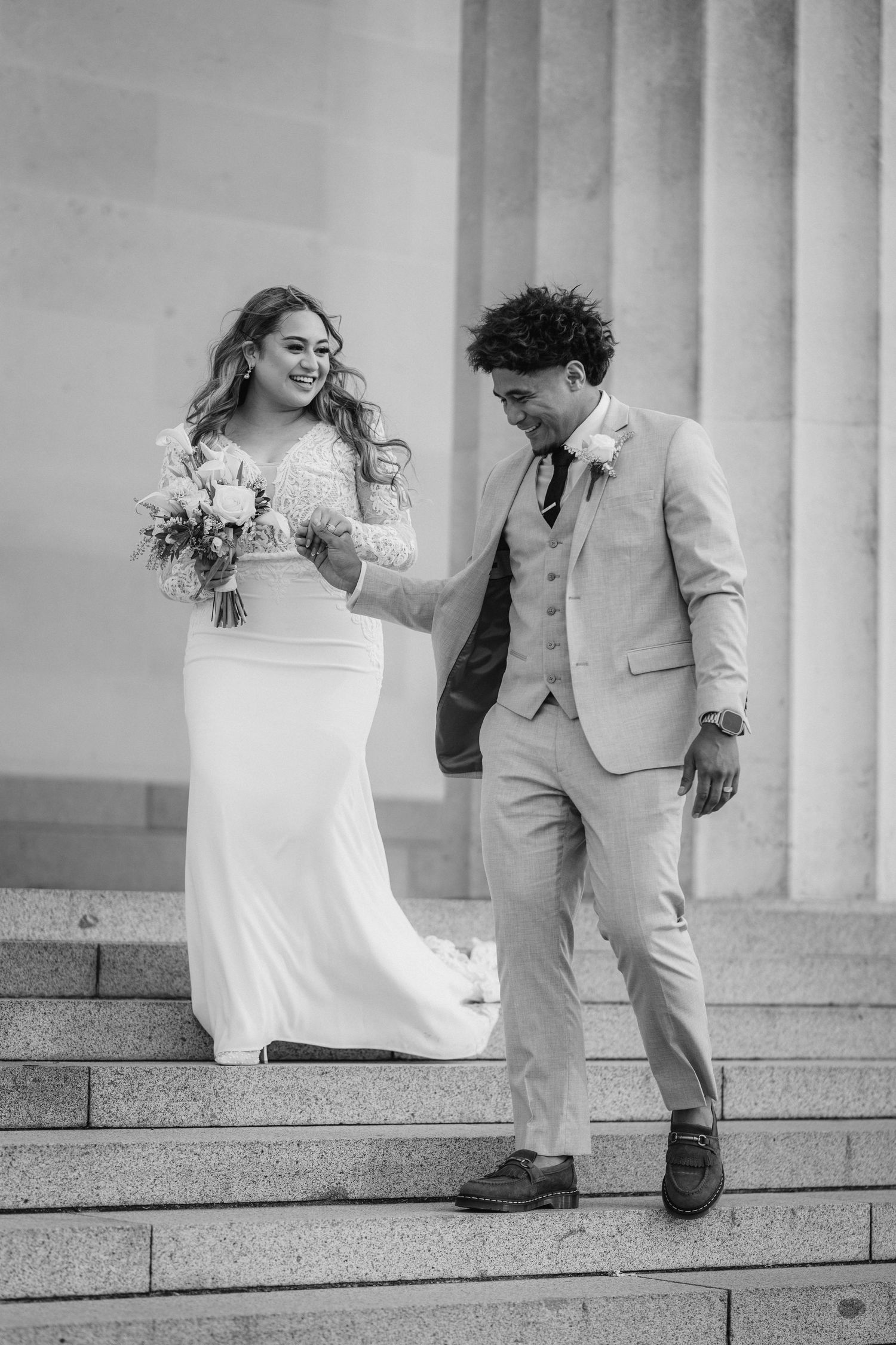 Wedding couple on stone steps with bride in white dress and groom in light colored suit.
