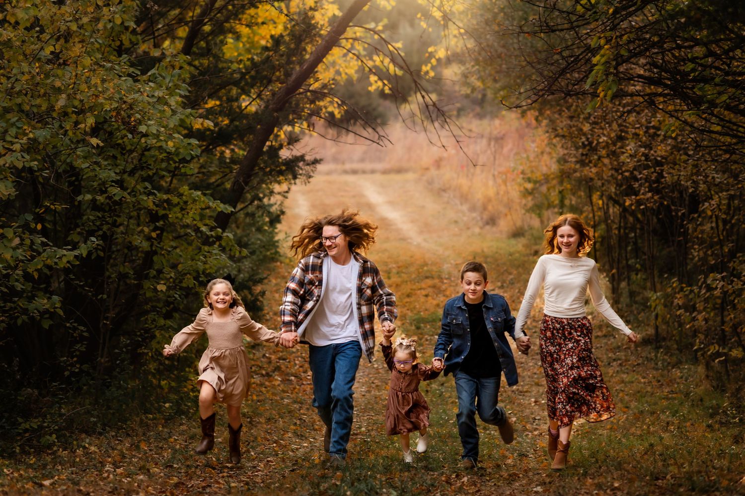 Group running joyfully together on a wooded autumn path with golden leaves and sunlight filtering through trees.