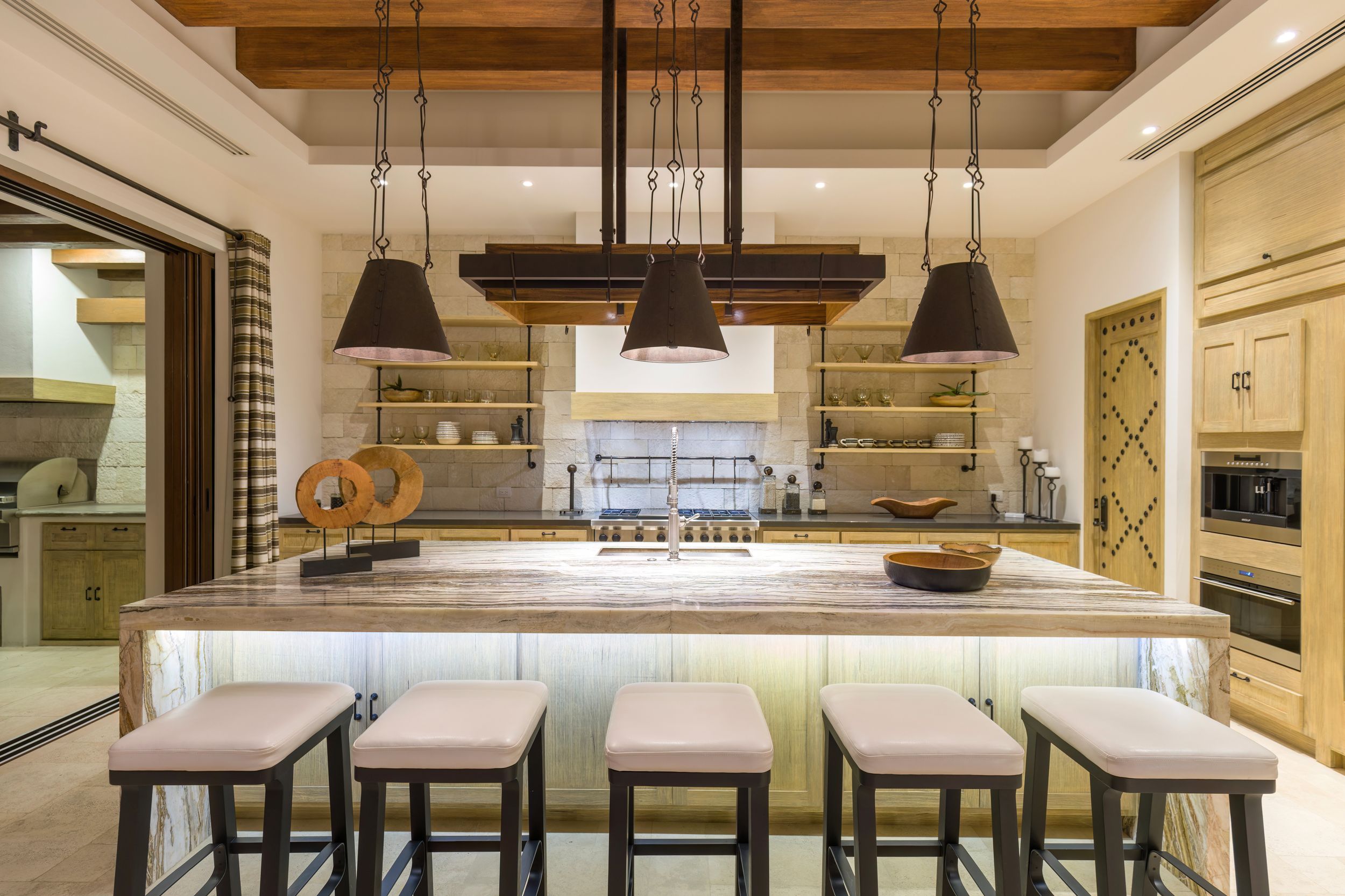 Modern kitchen interior with pendant lights, wood beams, and sleek white counter seating. Rancho San Lucas, Norman Estates.