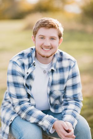 A person in a blue and white plaid flannel shirt and jeans sits outdoors during golden hour lighting.