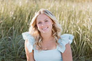 Portrait of a person in light blue ruffled dress smiling in a sunny field.