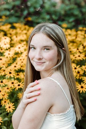 Portrait of someone in white against a backdrop of bright yellow Black-Eyed Susan flowers.