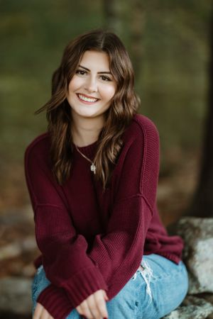 Casual portrait of someone in a burgundy sweater sitting outdoors.