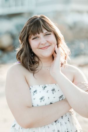 Portrait of someone in a floral dress smiling outdoors with soft lighting.