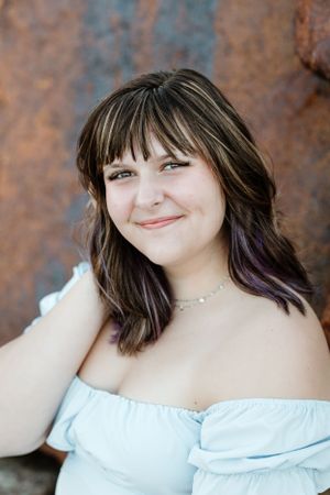 Portrait against a rustic background wearing an off-shoulder light blue dress.
