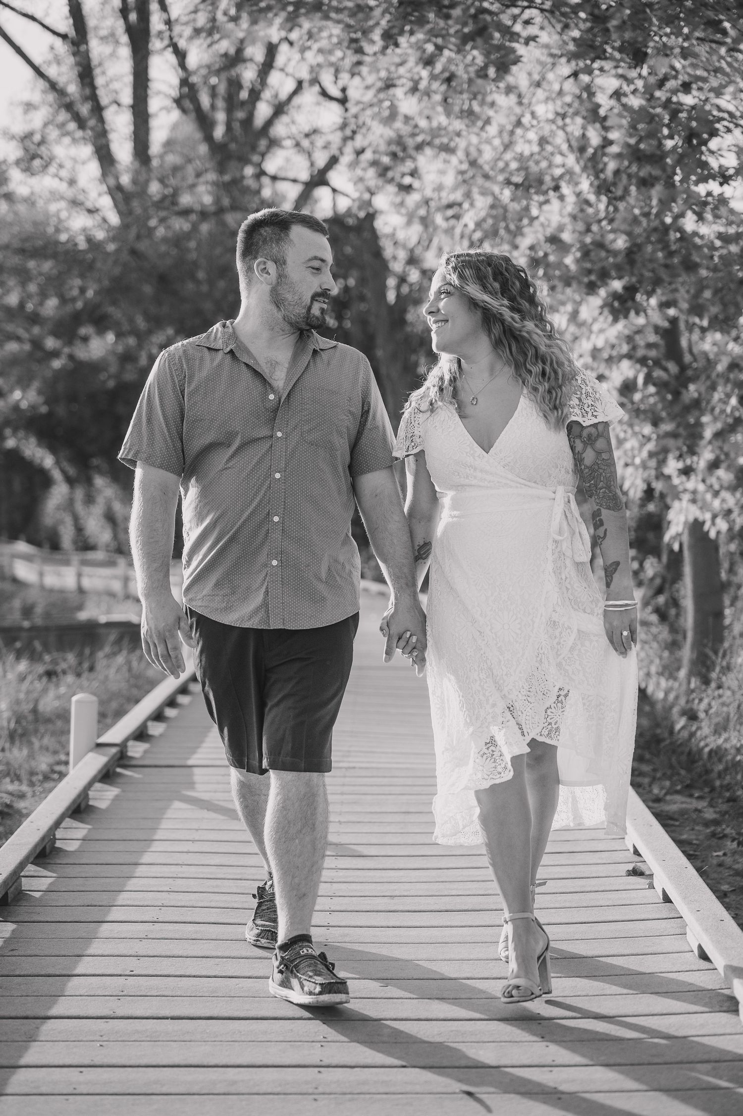 Couple walks hand in hand along a wooden boardwalk in casual wedding attire.