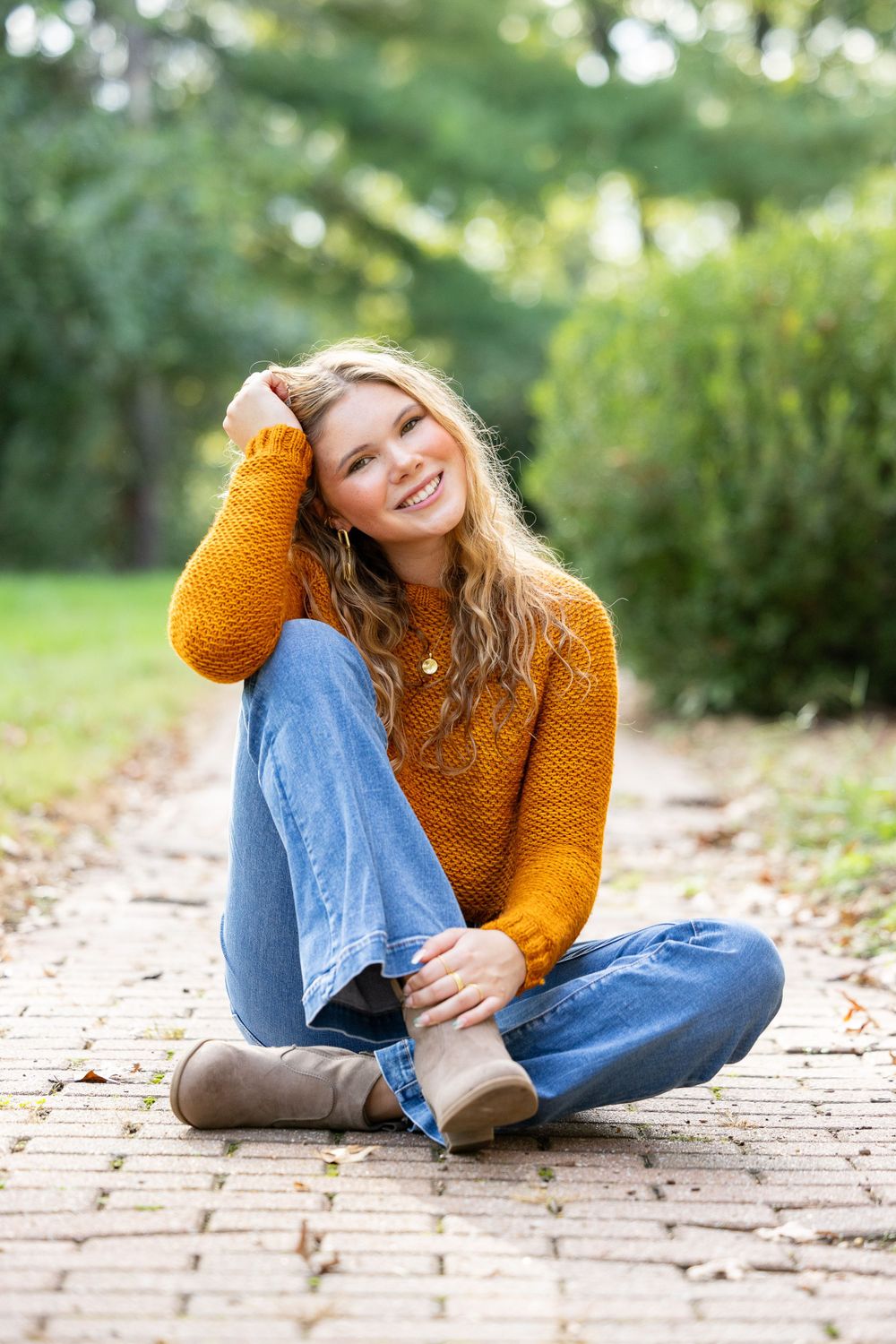 A young woman sitting on the ground in a field, smiling and enjoying the natural surroundings.