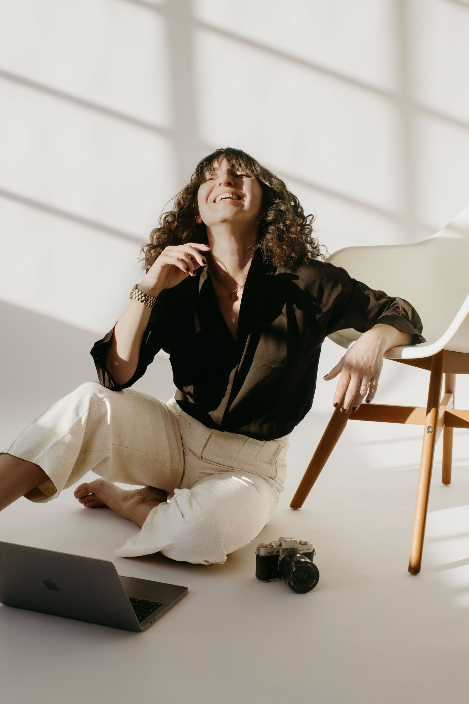 Stockholm event photographer sitting on a ground in a studio, leaning into a chair with her hand while sun shines on her face