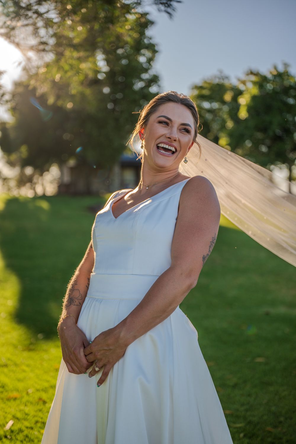 A radiant bride in classic white dress laughs in golden sunset light.