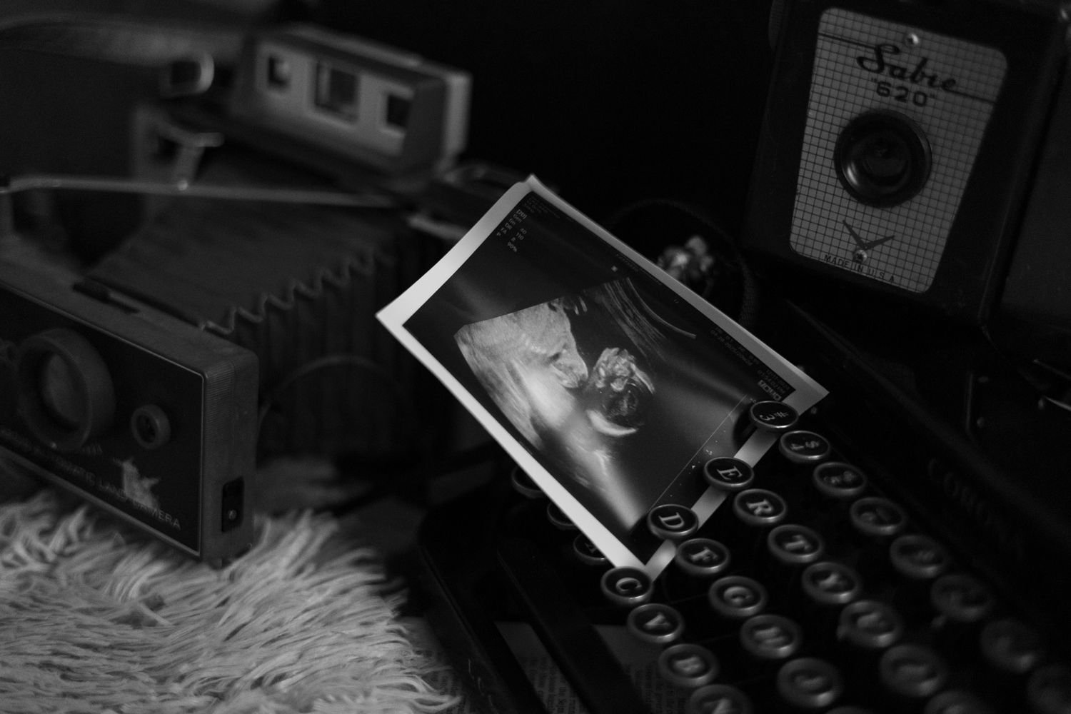A black and white still life with vintage cameras and a framed photograph on a textured surface.