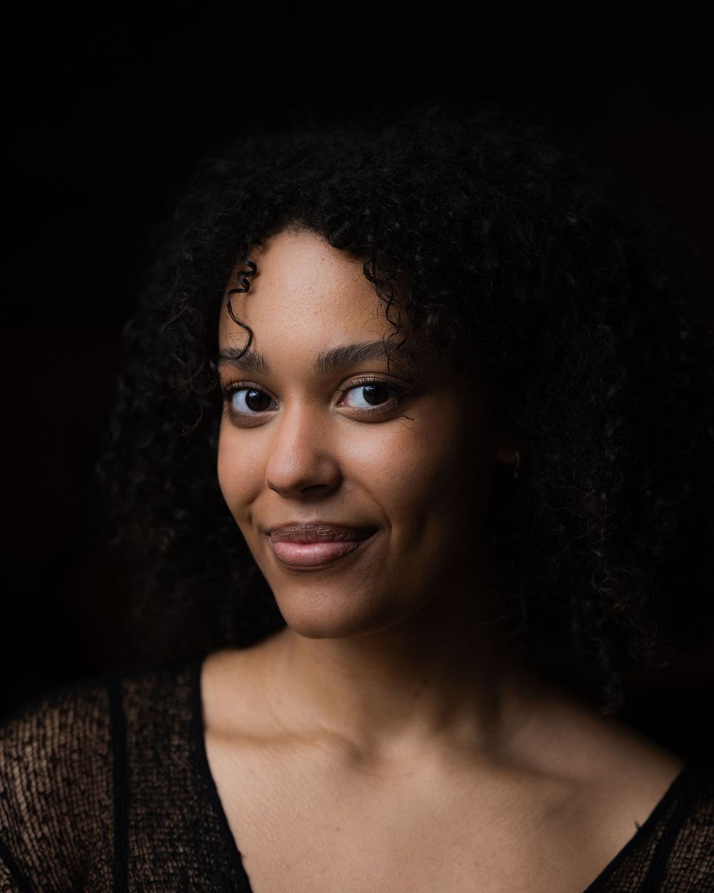 Striking portrait of a woman with curly hair, soft lighting, and a dark background—perfect for creative portfolios