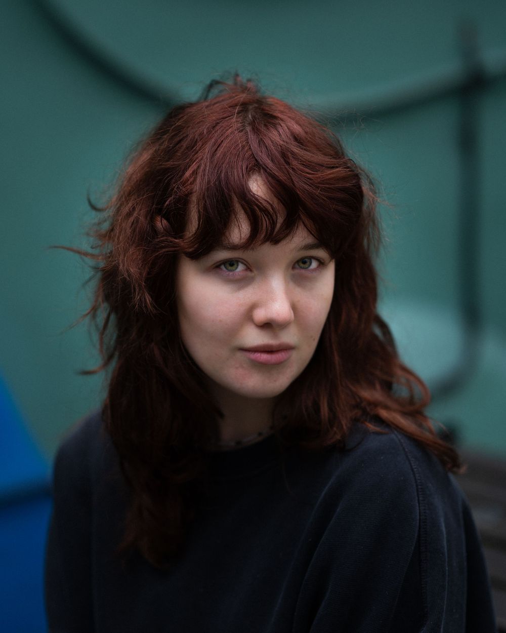 Natural headshot of a young woman with red hair, set against a soft teal background—capturing authenticity, emotion, and style.